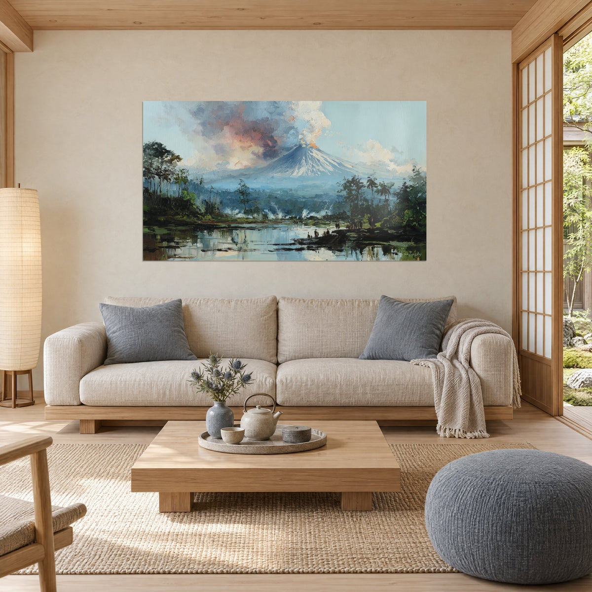 Wall art of a smoking snow-capped cone under a pale blue sky, pink and grey clouds, tropical lake reflected below, above a sofa in a bright living room