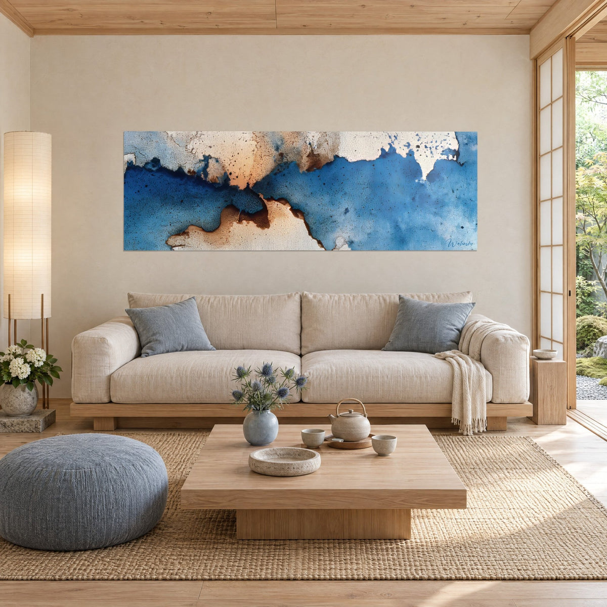Gemälde abstrakt in Kobaltblau und sandigem Beige mit zerklüfteten Rändern wie eine Küstenlinie, über einem Sofa in einem hellen Wohnzimmer
