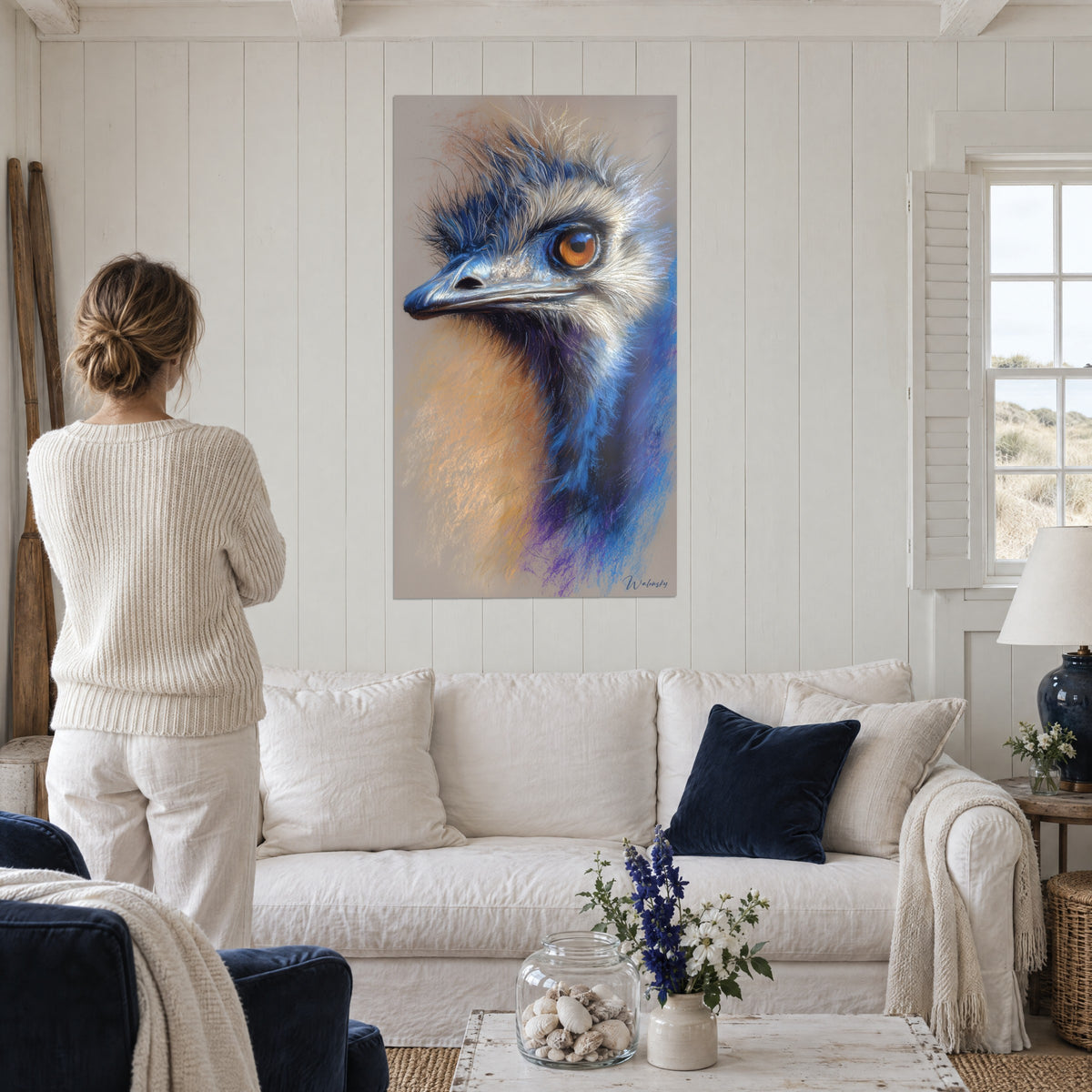 Wall art ostrich with orange eyes, cobalt blue and sand plumage, seen from behind above a sofa in a bright living room