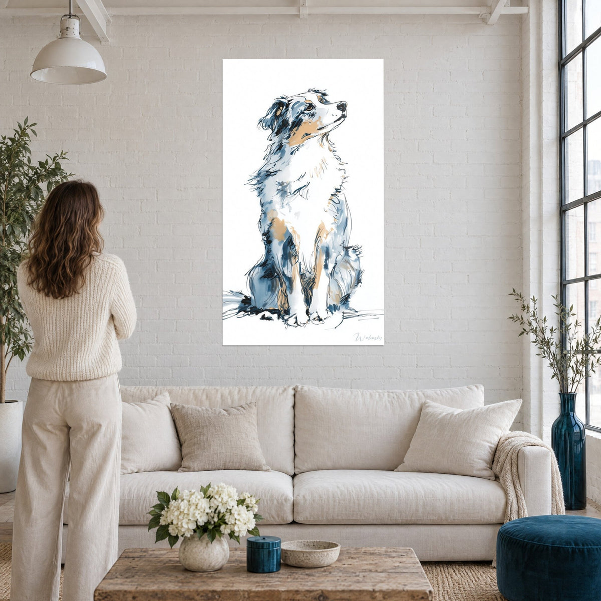 Wall art of a sheepdog with slate blue and honey patches, sitting and gazing upward, above a sofa in a bright living room