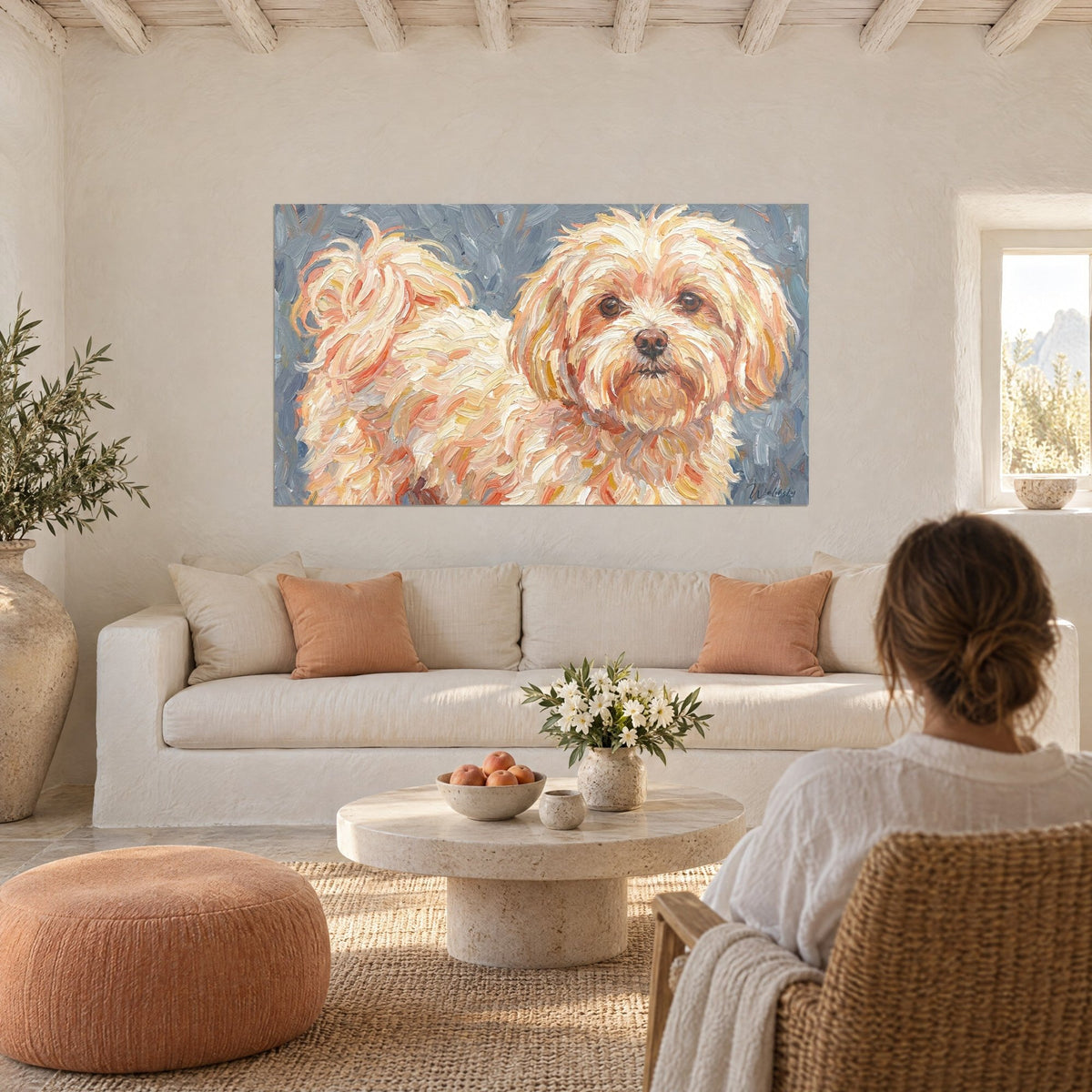Cuadro pequeño perro crema de pelo rizado, toques albaricoque y reflejos cobrizos sobre fondo gris azulado, mujer de espaldas, encima de un sofá en un salón luminoso