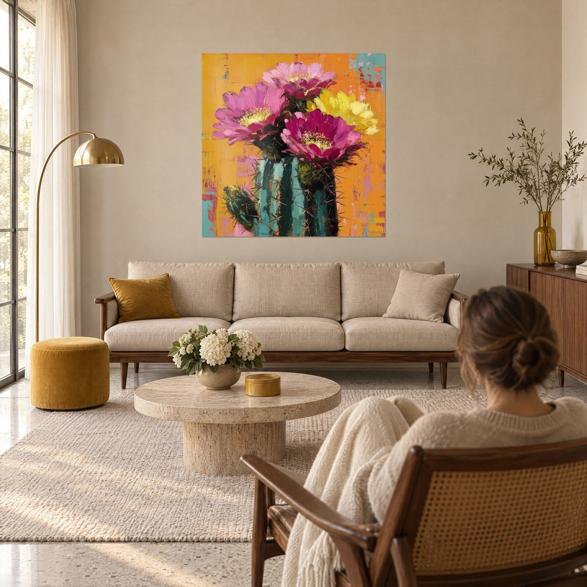 Gemälde Kakteen mit blühenden Blüten in Rosa und Zitronengelb auf leuchtend orangefarbenem Hintergrund, über einem Sofa in einem hellen Wohnzimmer
