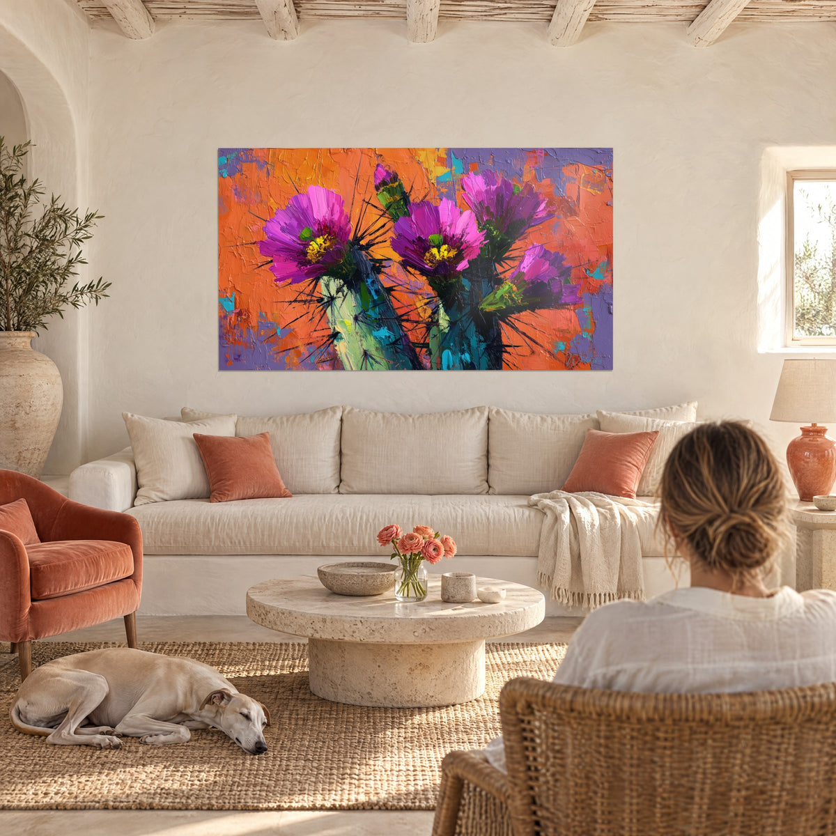 Cuadro cactus en flor con pétalos magenta y corazón amarillo sobre fondo naranja, encima de un sofá en un salón luminoso