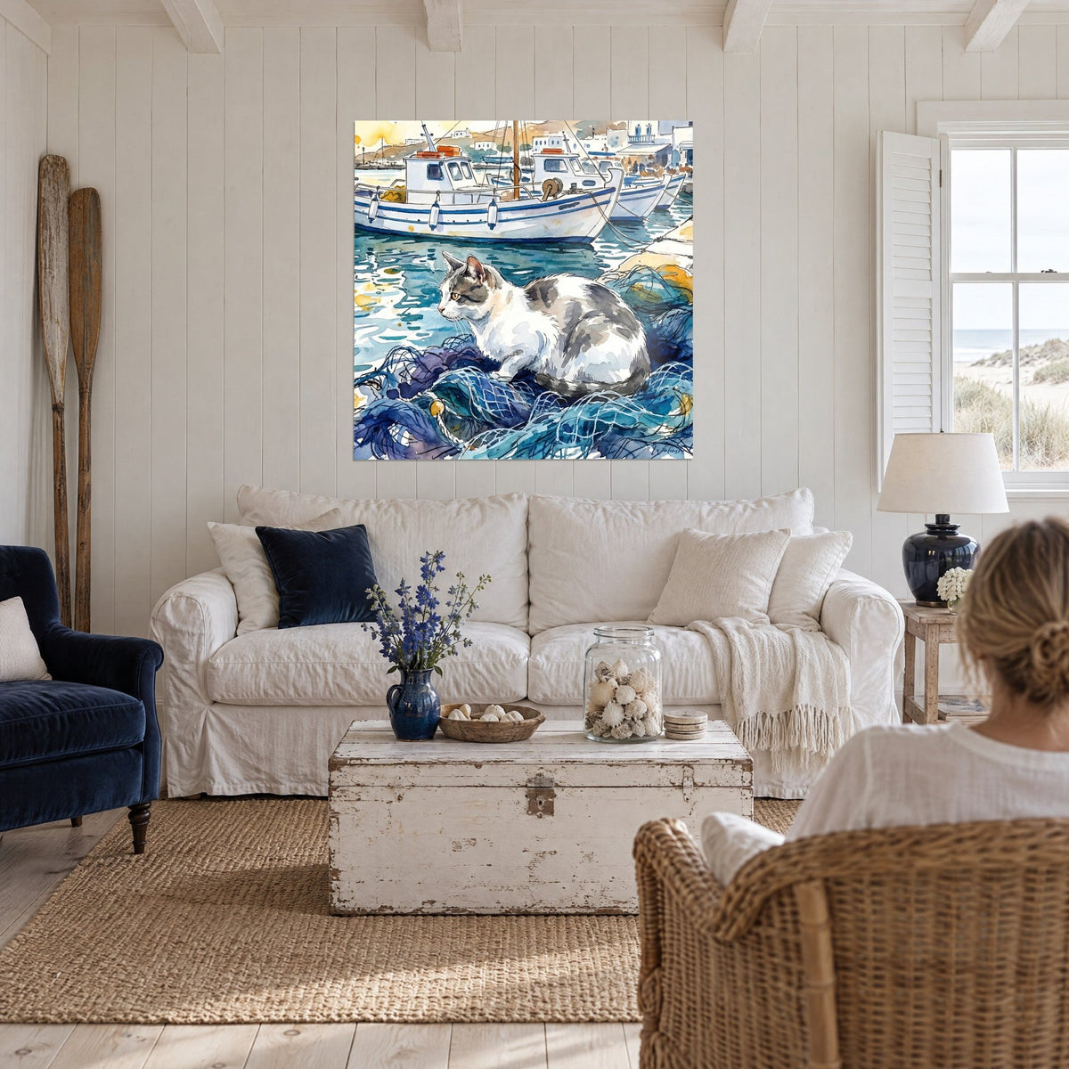 Schilderij witte en grijze gestreepte kat opgekruld op blauwe visnetten, vissersboten op de achtergrond, boven een bank in een lichte woonkamer
