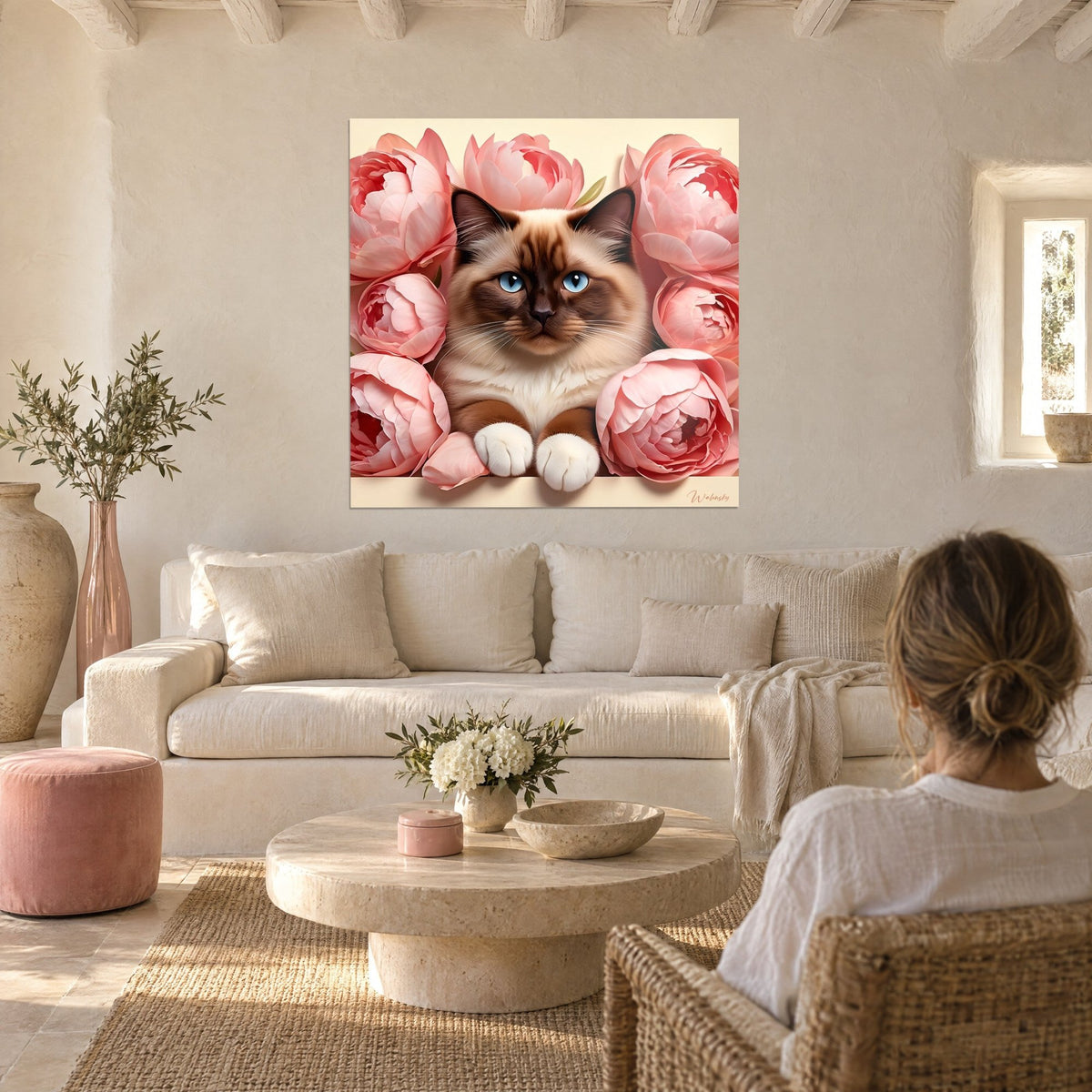 Wall art Siamese kitten with blue eyes surrounded by powder pink peonies, white paws, above a sofa in a bright living room
