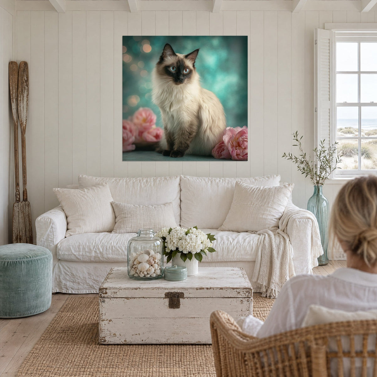 Tableau chat balinais aux yeux bleus, masque brun et pivoines roses sur fond turquoise, au-dessus d'un canapé dans un salon lumineux