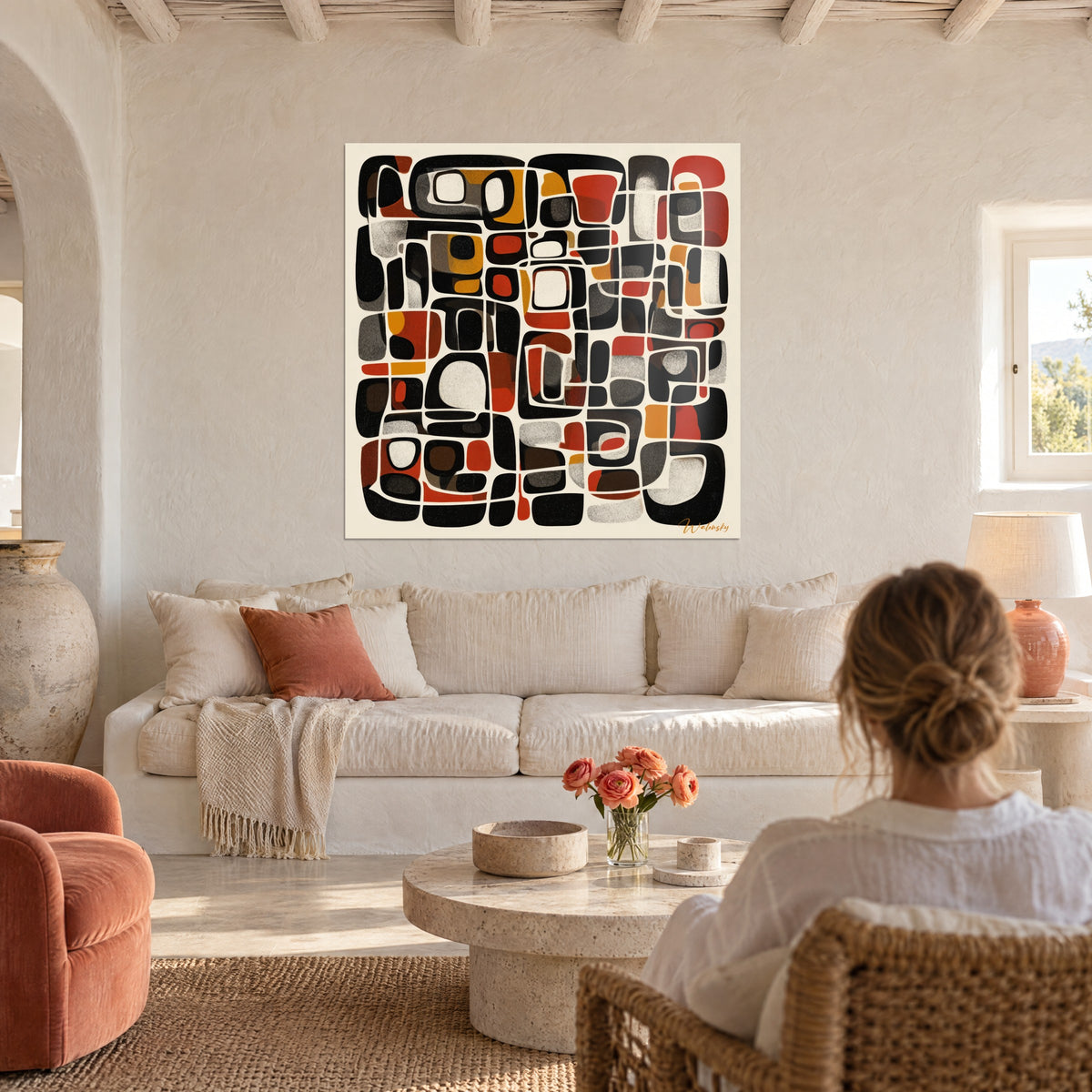 Wall art mosaic of rounded black, rust and ochre blocks on a cream background, woman seen from behind above a sofa in a bright living room
