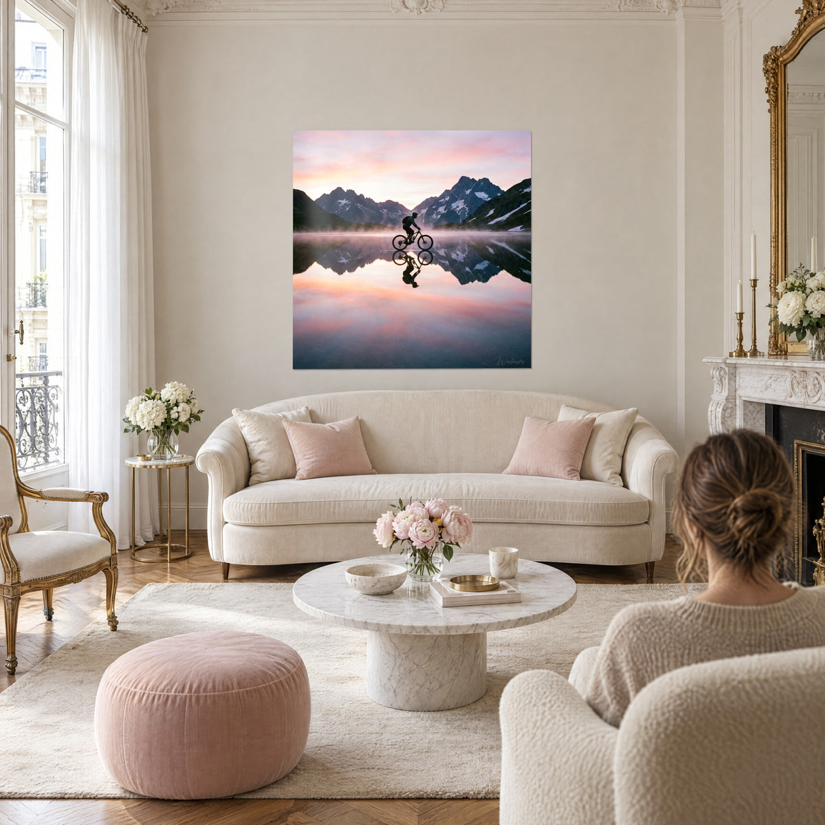 Schilderij fietser in silhouet op een spiegelmeer, roze en oranje lucht, besneeuwde toppen, boven een bank in een lichte woonkamer