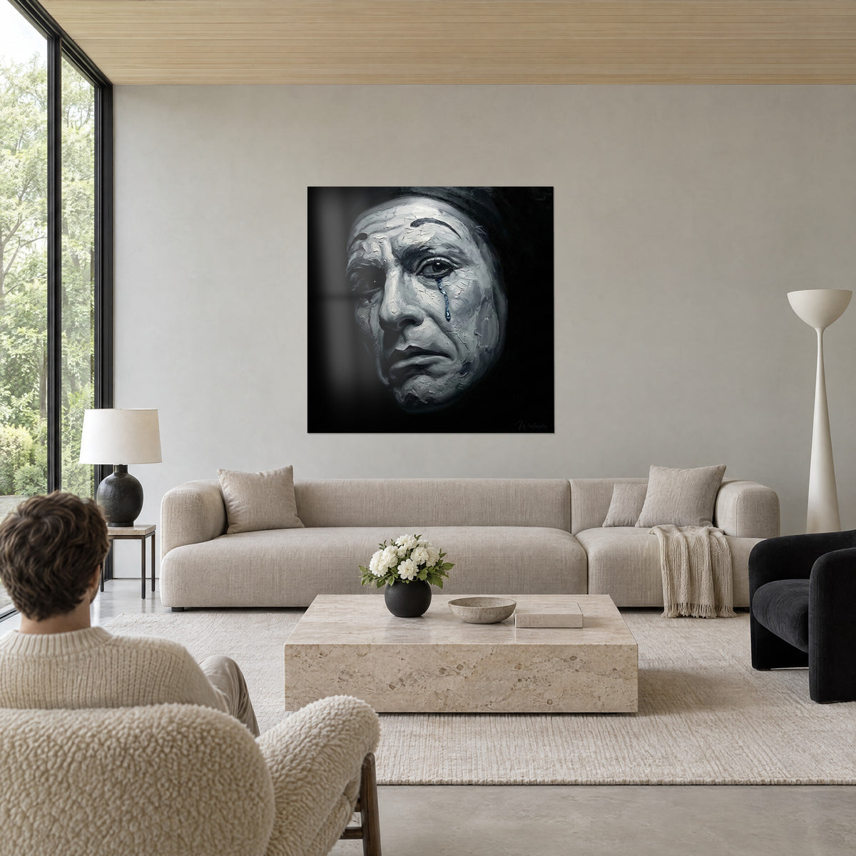 Tableau visage de clown aux larmes bleues, peinture à la spatule grise et blanche sur fond noir, au-dessus d'un canapé dans un salon lumineux