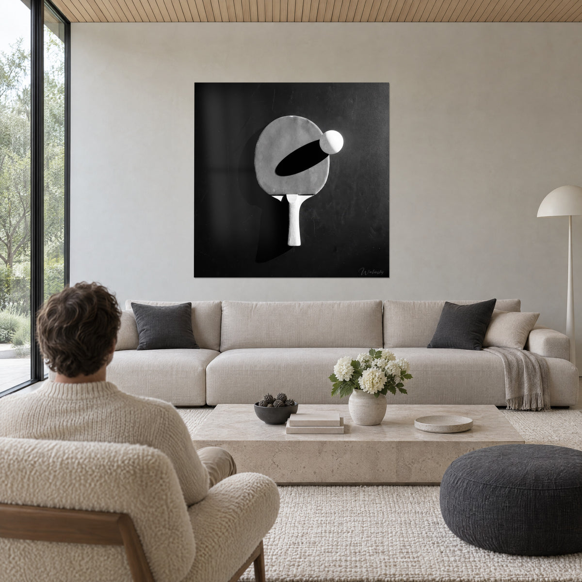 Πίνακας με γκρι ρακέτα ping-pong και λευκή μπάλα, μαύρη σκιά, φόντο χρώματος σχιστόλιθου, πάνω από καναπέ σε φωτεινό σαλόνι