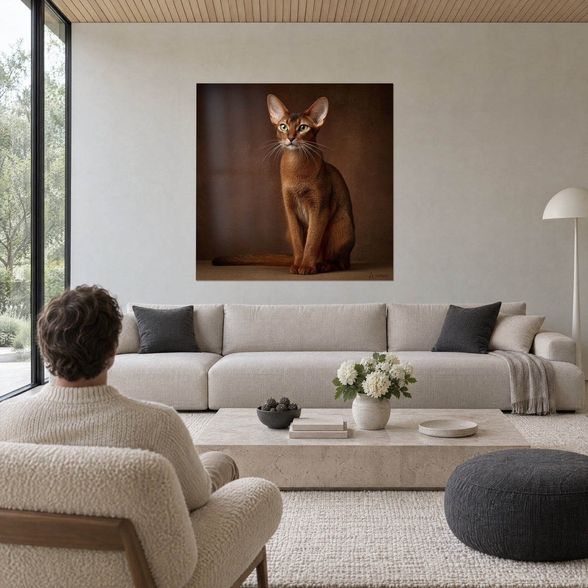 Wall art ruddy Abyssinian cat with green eyes, seated on a brown background, two people seen from behind, above a sofa in a bright living room