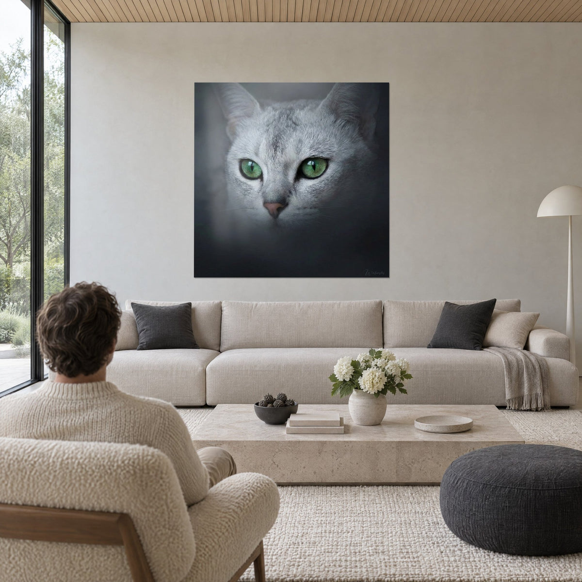 Schilderij zilverkleurige Burmilla-kat met groene ogen, roze snuit en antracietkleurige achtergrond, een man van achteren, boven een bank in een lichte woonkamer