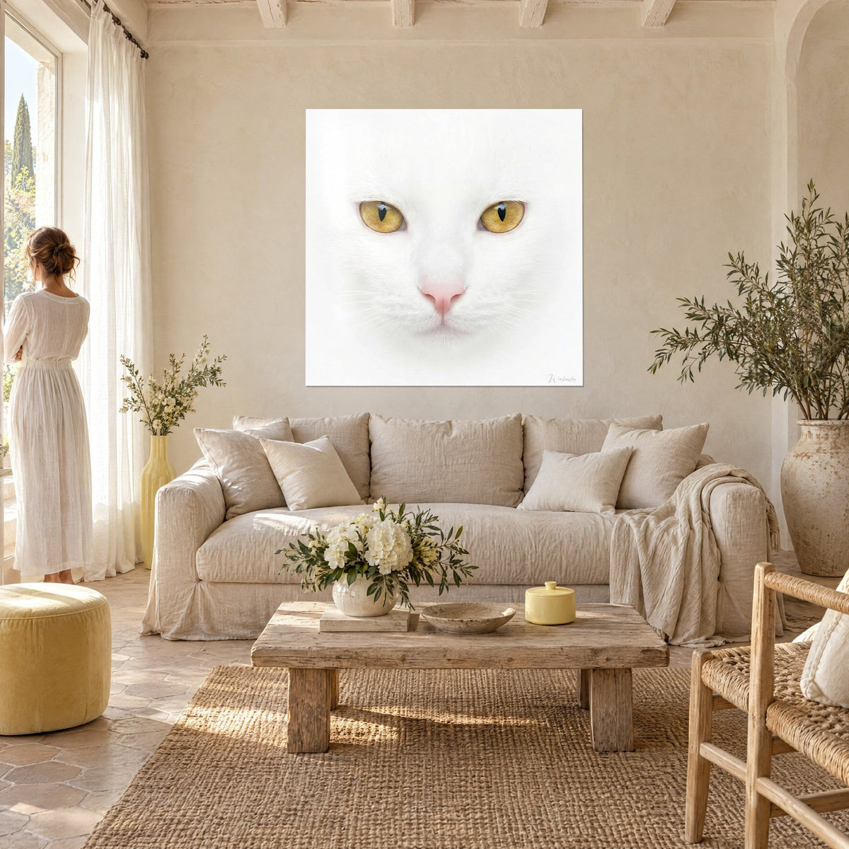 Schilderij portret van een brandschone witte kat, barnsteenkleurige ogen en roze neus, een vrouw in witte jurk van achteren boven een bank in een lichte woonkamer