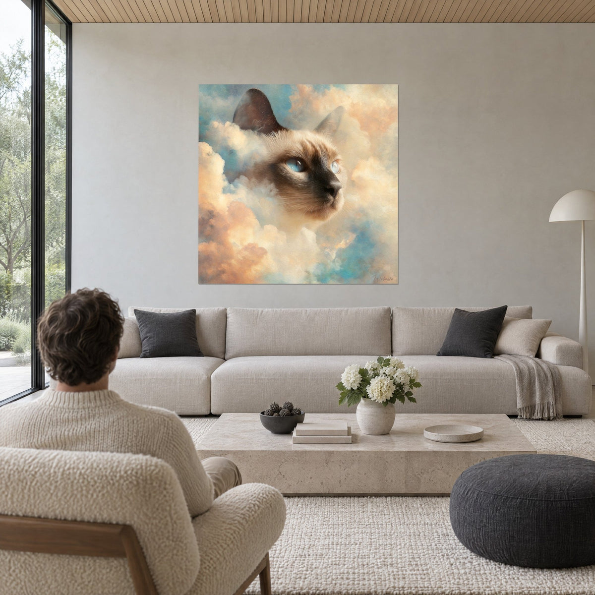 Wall art Tonkinese cat with blue eyes emerging from cream and coral clouds, person seen from behind, above a sofa in a bright living room