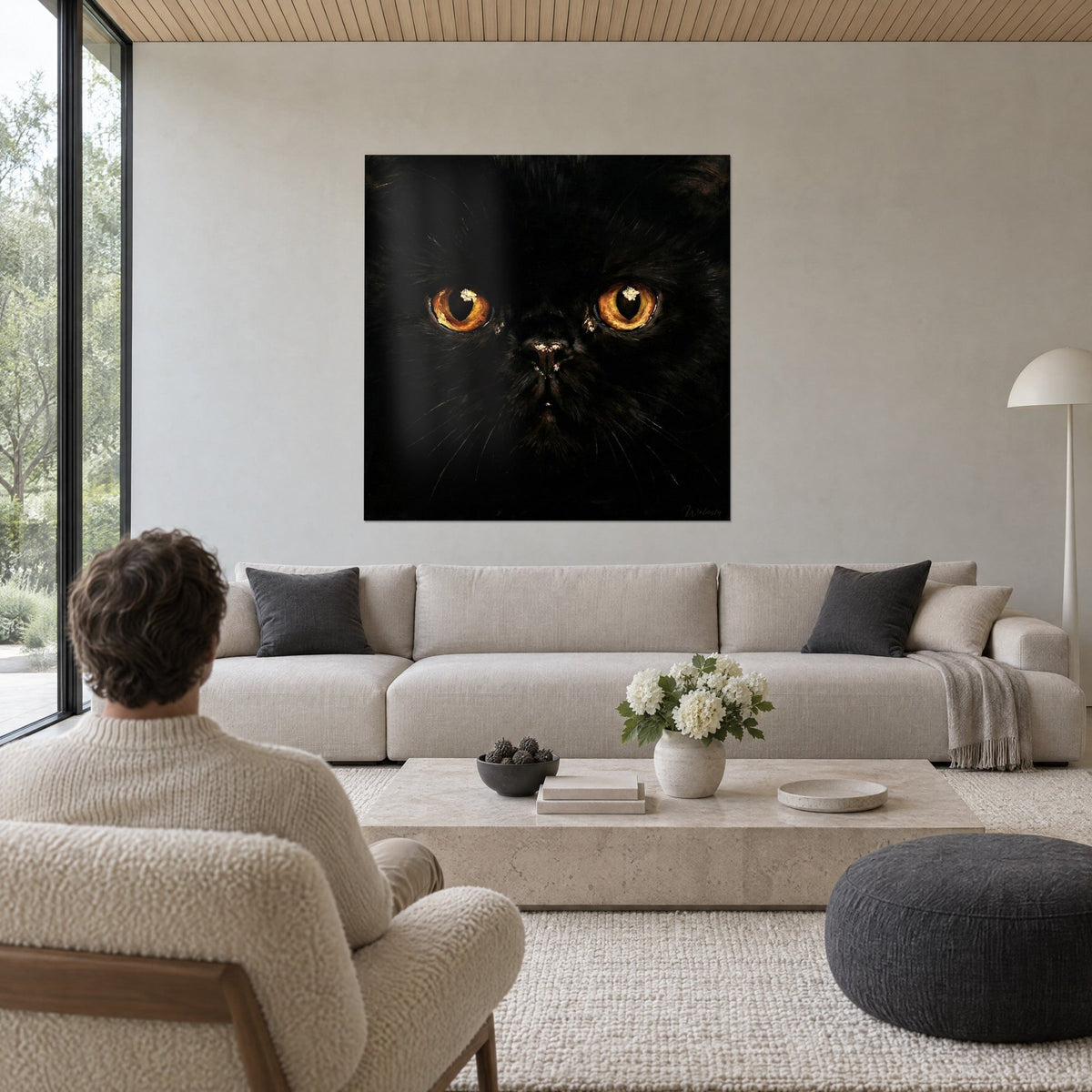 Tableau portrait félin noir aux iris ambrés lumineux, homme de dos, au-dessus d'un canapé dans un salon lumineux
