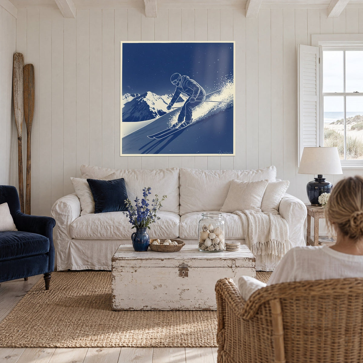 Quadro di uno sciatore piegato in piena discesa, blu notte e bianco crema, scia di neve farinosa, sopra un divano in un soggiorno luminoso