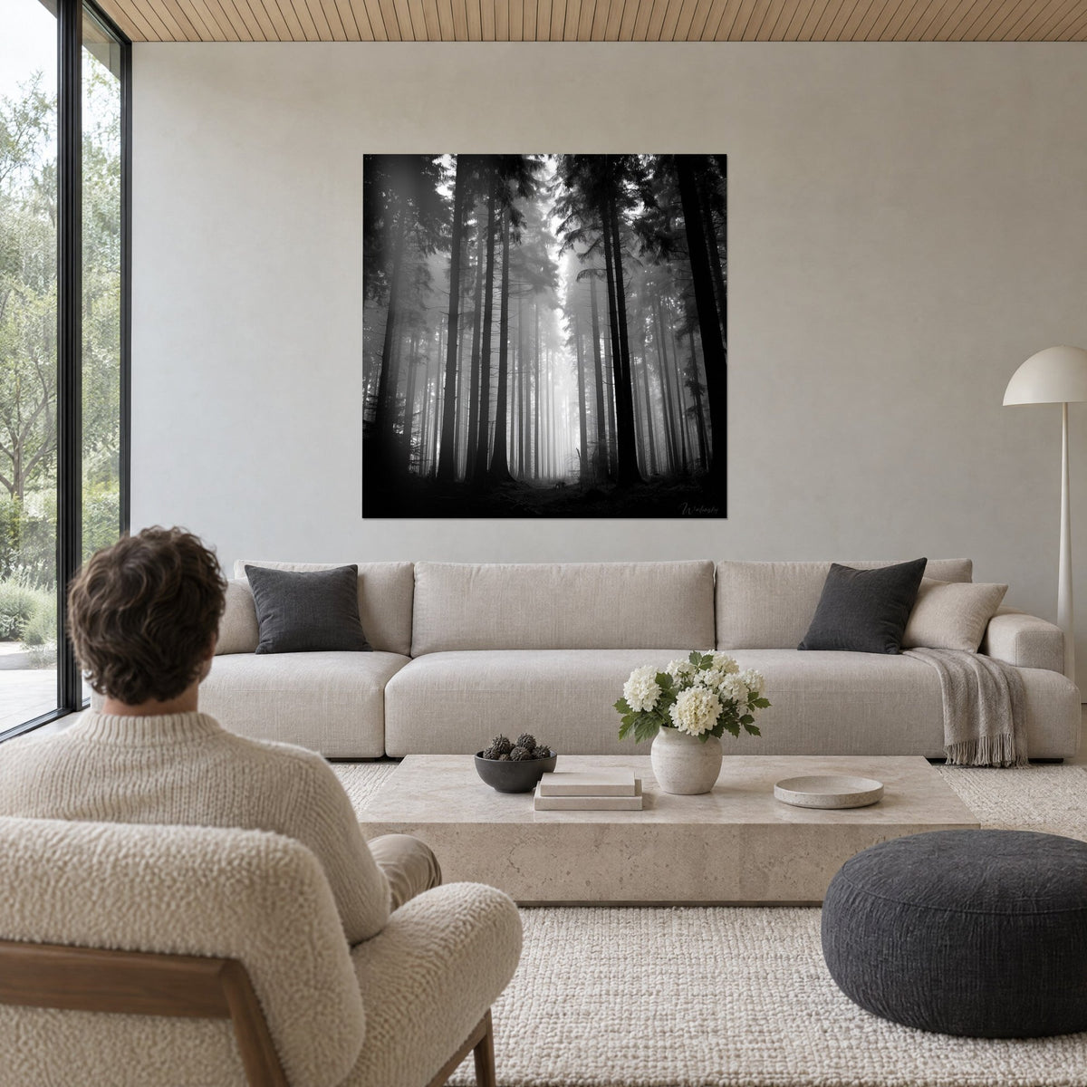 Gemälde schlanke Tannen im Nebel versunken, tiefes Schwarz und Perlgrau, ein Mann von hinten, über einem Sofa in einem hellen Wohnzimmer