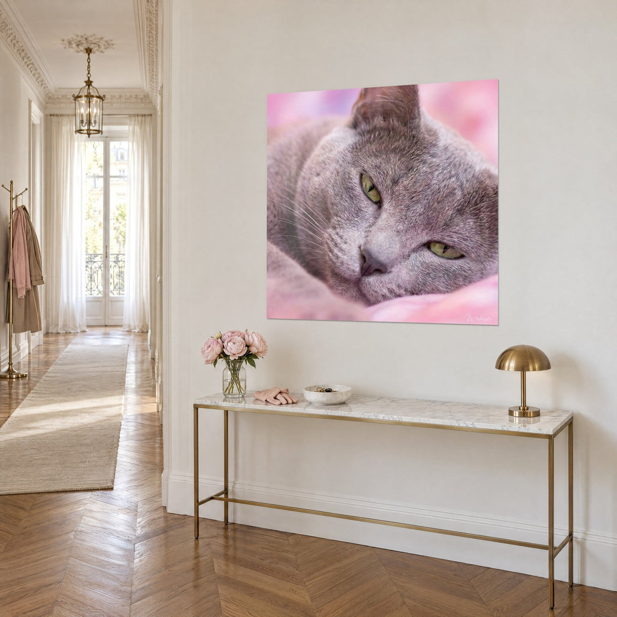 Cuadro felino gris lavanda con pupilas verde tilo, hocico rosado sobre fondo empolvado, colgado encima de una consola dorada, vista de tres cuartos