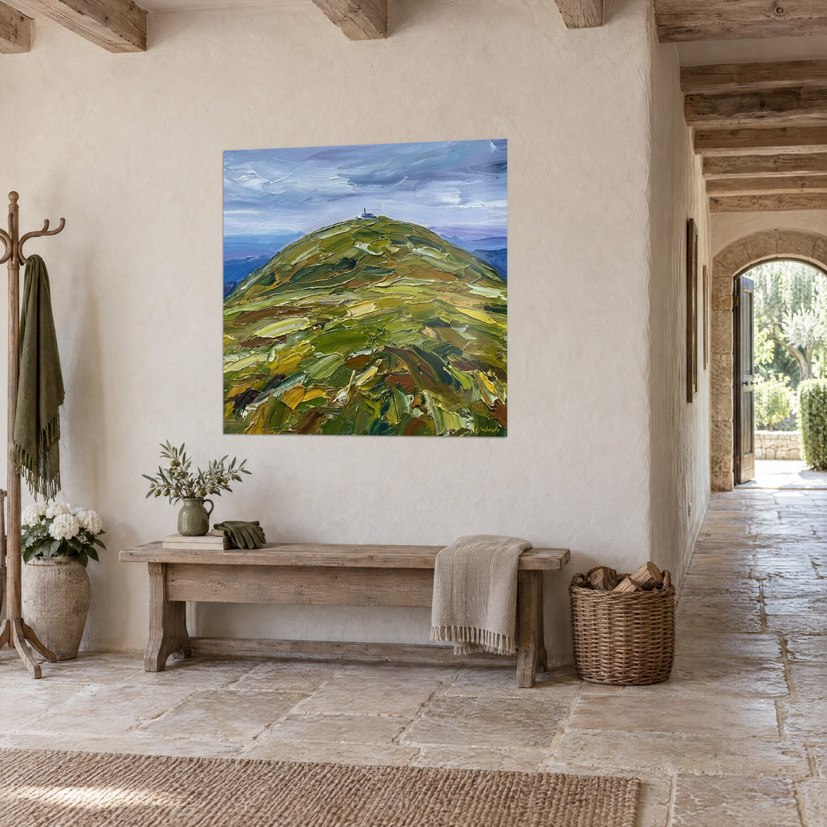 Quadro montagna arrotondata nelle tonalità oliva e rame che contrastano con le montagne azzurrate sullo sfondo, vista di tre quarti in un ingresso in pietra