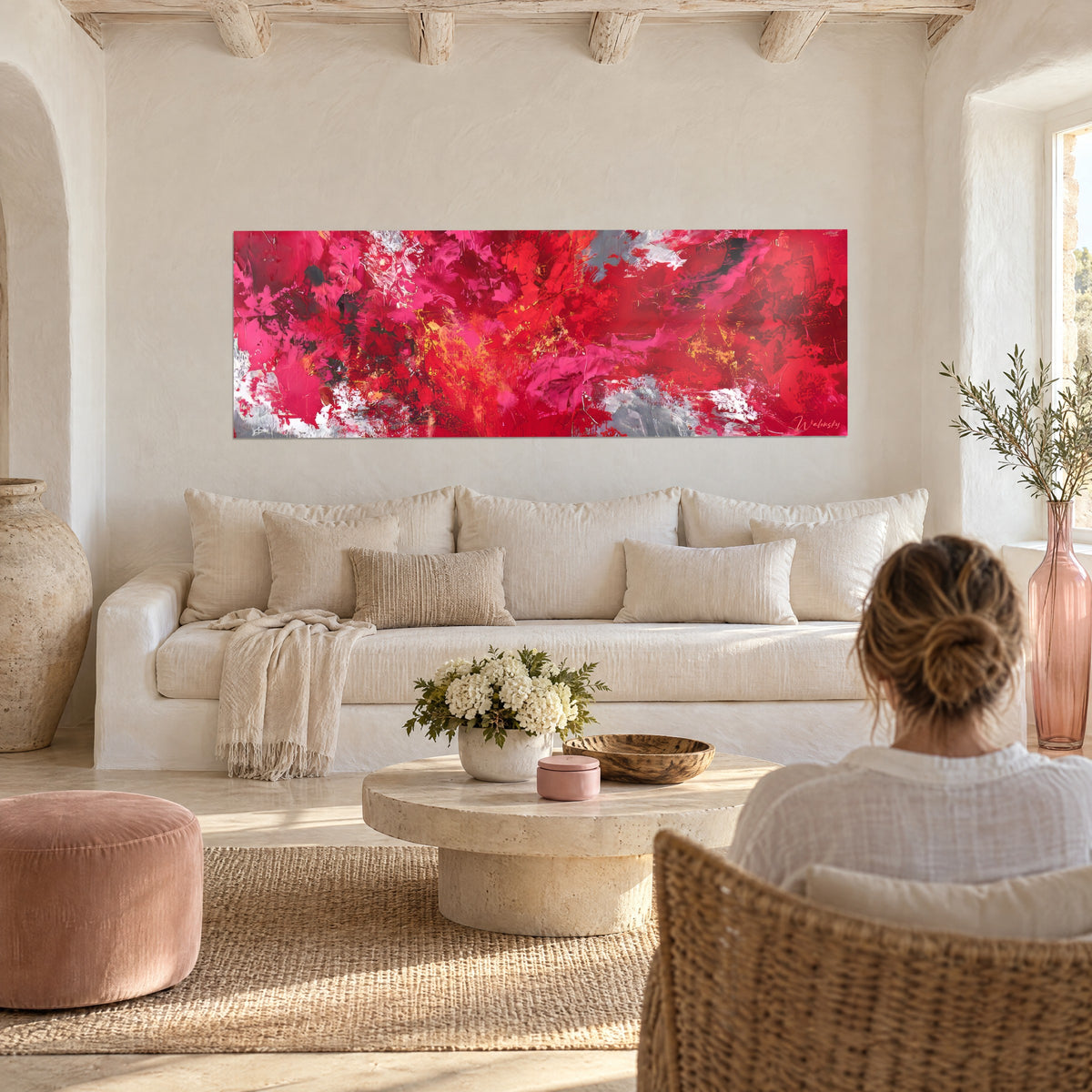 Wall art explosion of carmine red and fuchsia pink with grey accents, woman seen from behind, above a sofa in a bright living room