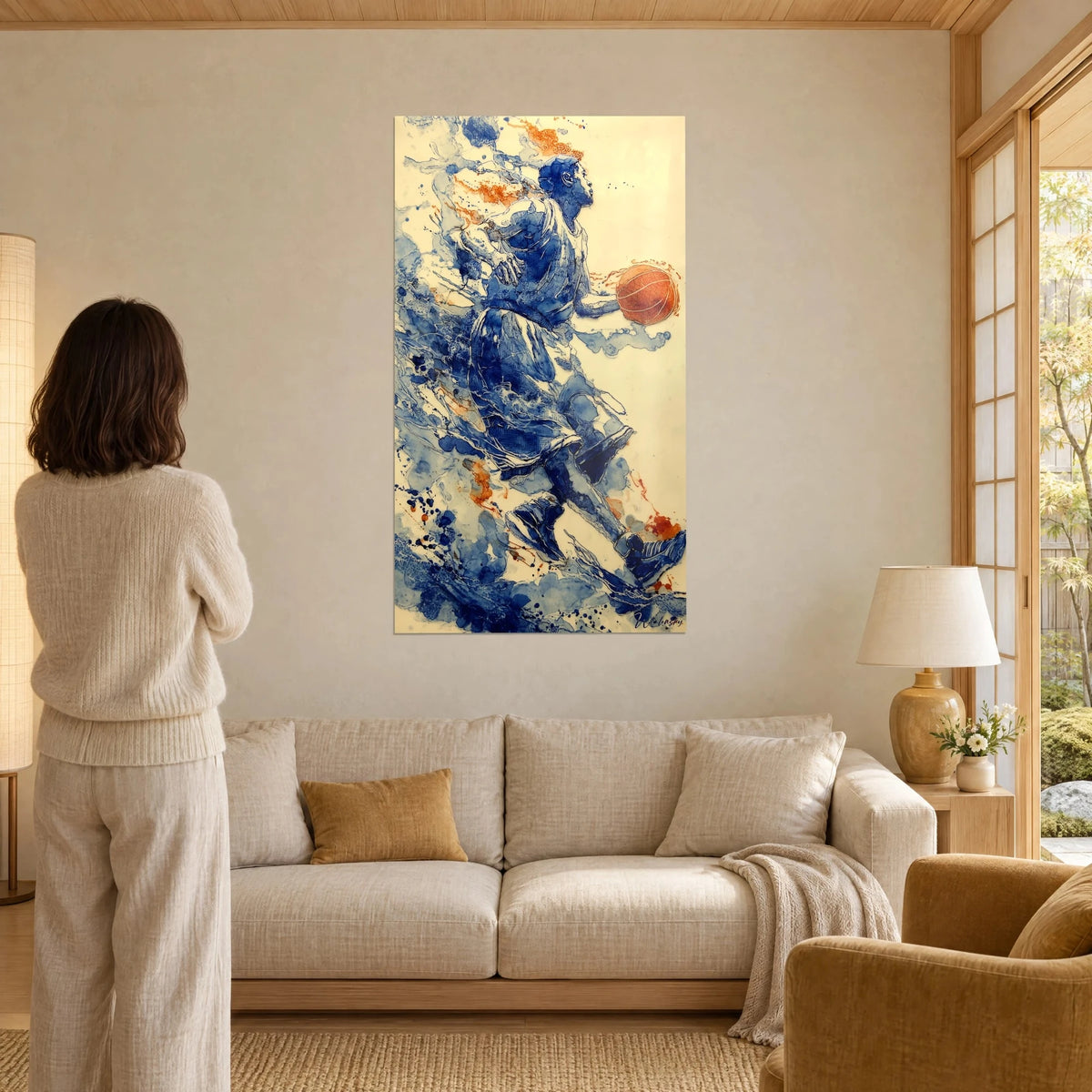 Schilderij van een basketballer in kobaltblauw in volle sprint, oranje bal in de hand, spatten, vrouw van achteren, boven een bank in een lichte woonkamer