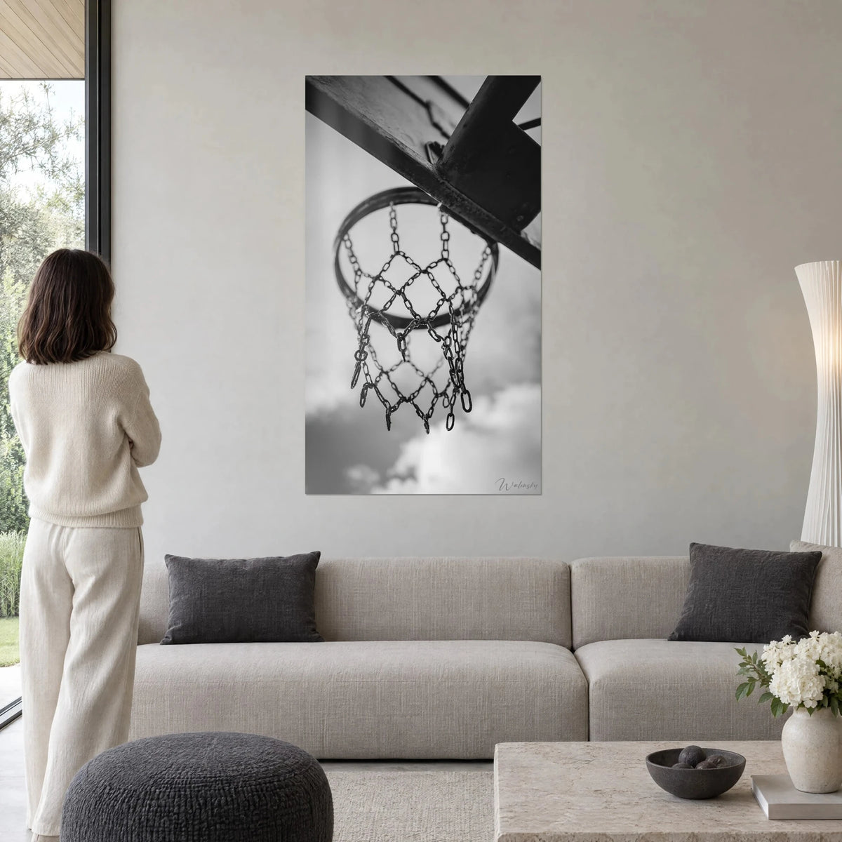 Gemälde Basketballkorb mit verrosteten Ketten vor grauem und weißem Wolkenhimmel, Frau von hinten, über einem Sofa in einem hellen Wohnzimmer