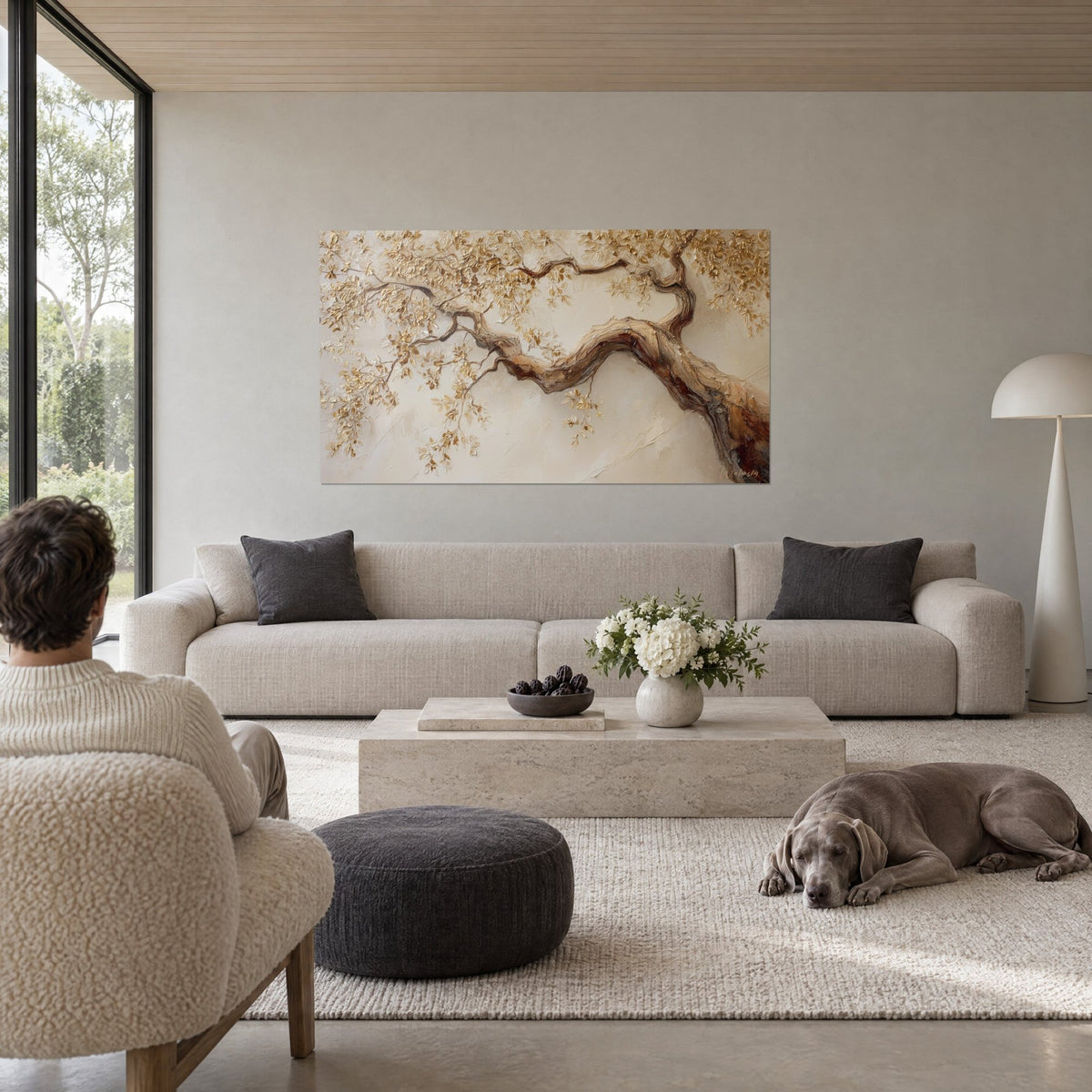 Tableau branche dorée aux feuilles en relief, tronc brun et fond beige crème, au-dessus d'un canapé dans un salon lumineux
