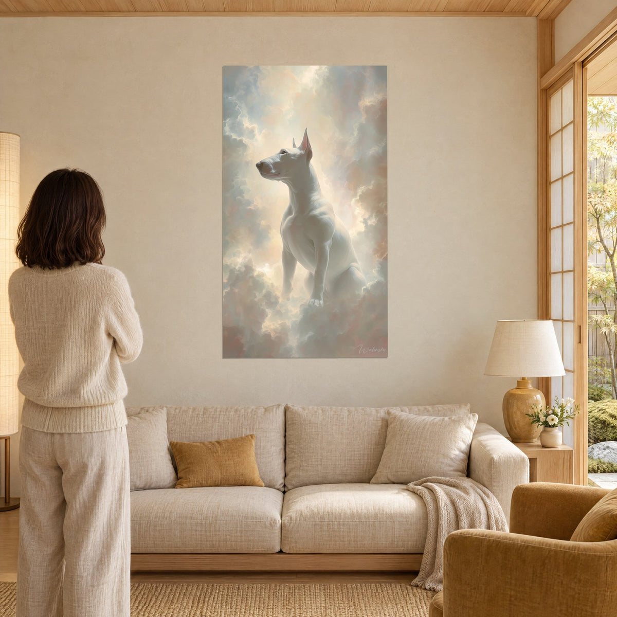 Πίνακας λευκός bull terrier καθισμένος σε ροζ και χρυσά σύννεφα, με το βλέμμα στο φως, πάνω από έναν καναπέ σε φωτεινό σαλόνι