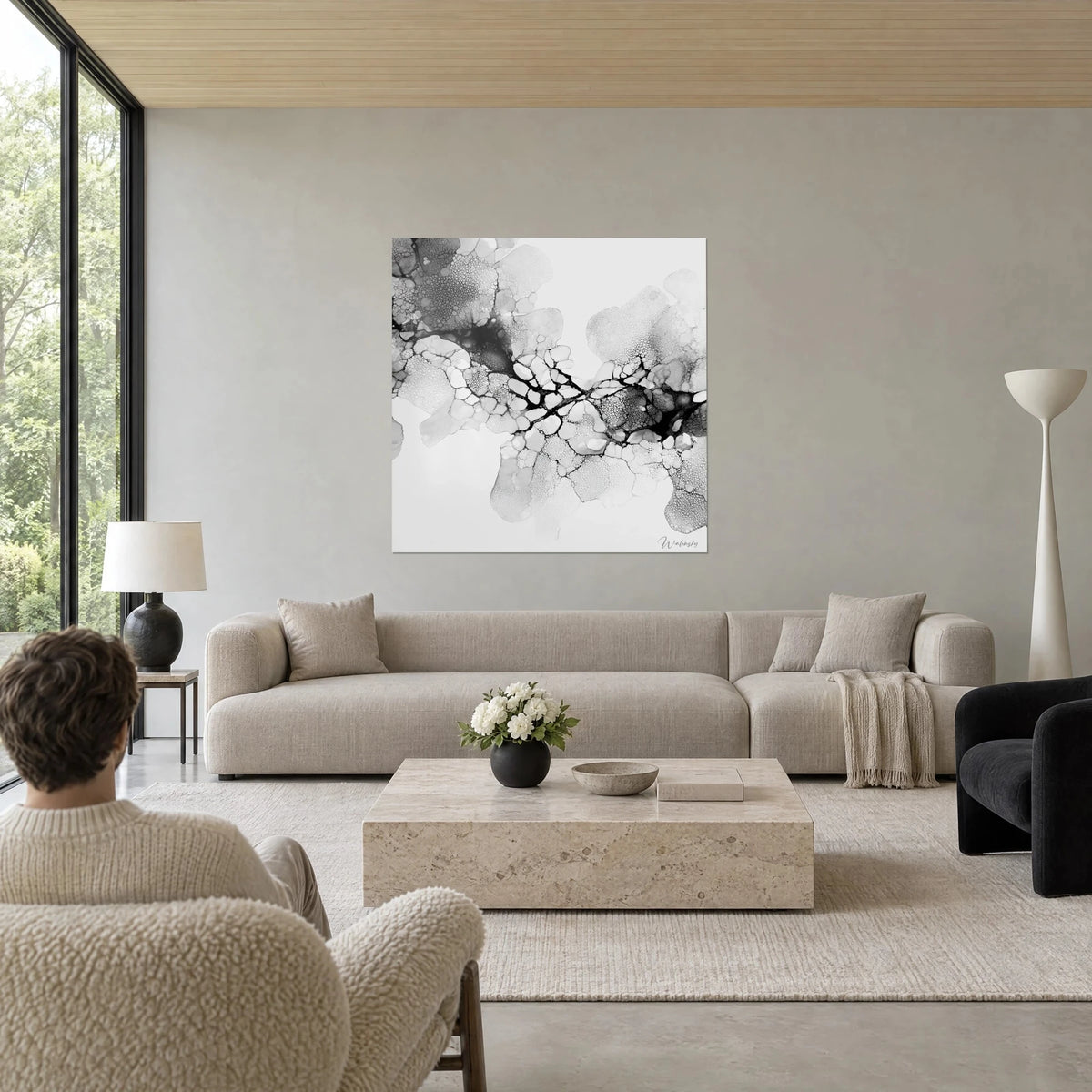 Wall art with grey organic cells, black crack network on white background, a person seen from behind, above a sofa in a bright living room