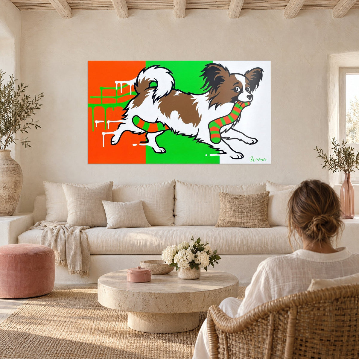 Quadro di cane farfalla che balza, pelo marrone e bianco, calzino a righe arancio e verdi in bocca, sopra un divano in un soggiorno luminoso