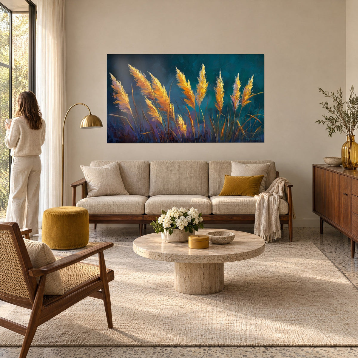 Gemälde Pampagras-Ähren in Gold, vom Wind gestreift, auf blaugrünem Hintergrund, gegenüber einer Frau von hinten, über einem Sofa in einem hellen Wohnzimmer