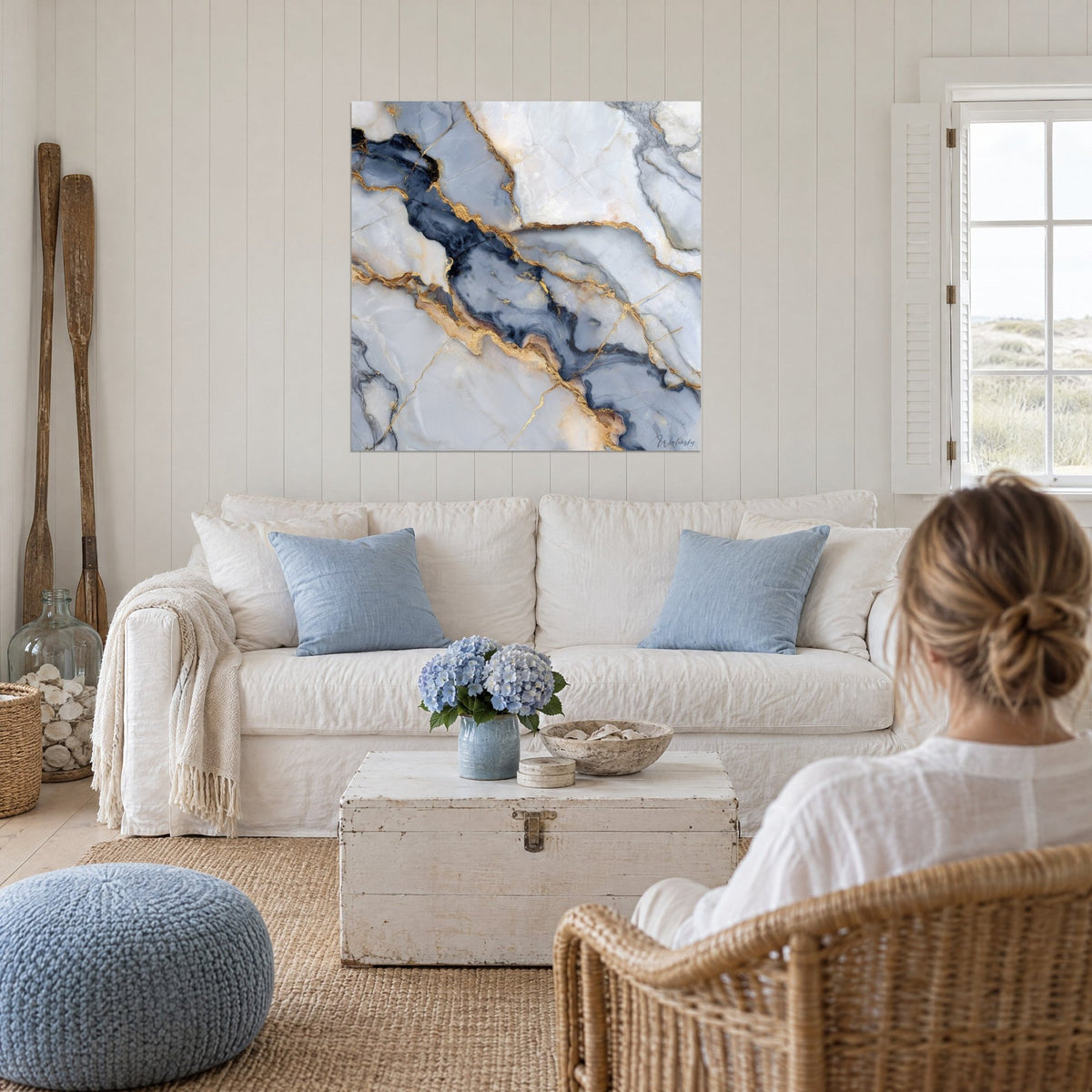 Tableau marbre bleu nuit veiné d'or étendu sur le mur blanc, femme de dos, au-dessus d'un canapé dans un salon lumineux