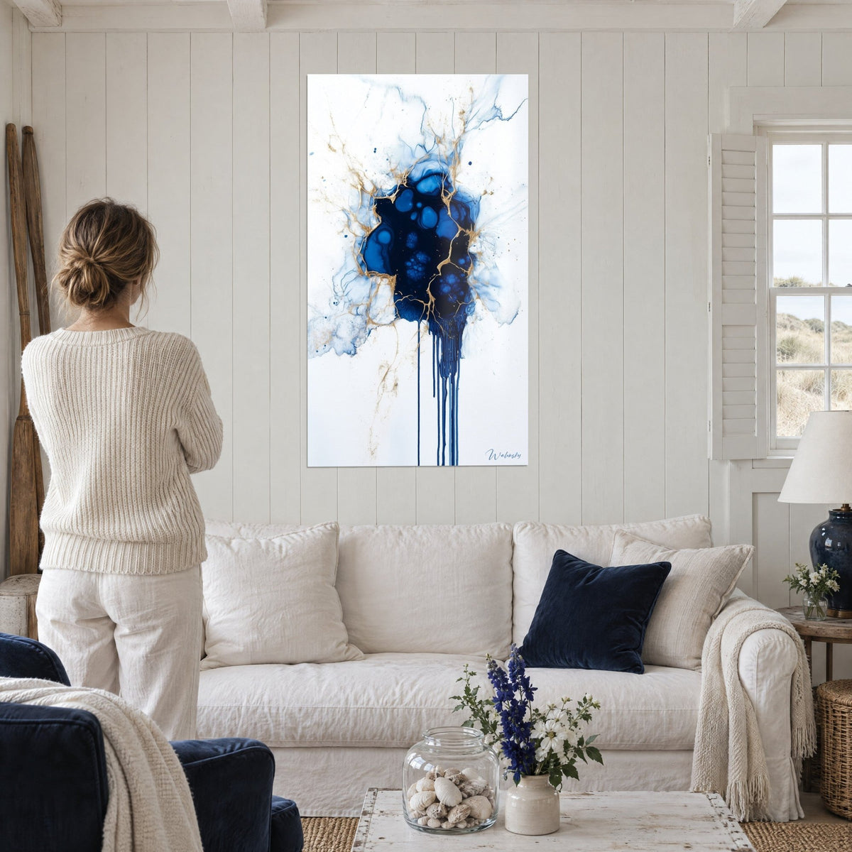 Wall art midnight blue and gold ink explosion, golden veins on a white background, woman from behind above a sofa in a bright living room