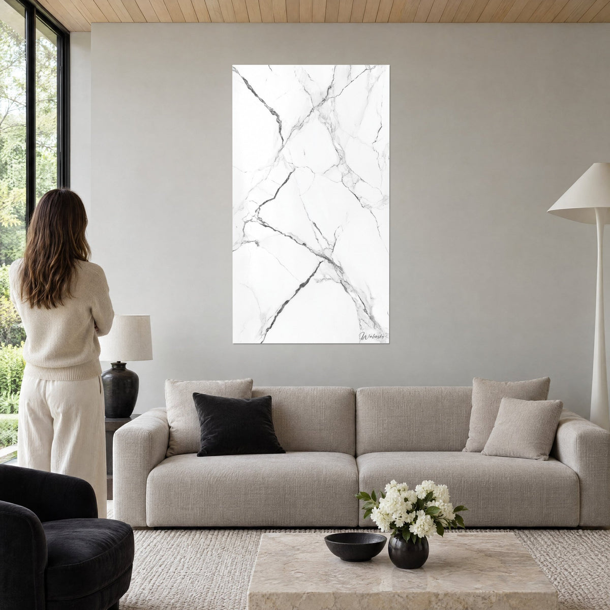 Tableau marbre blanc veiné de gris anthracite, femme de dos devant, au-dessus d'un canapé dans un salon lumineux
