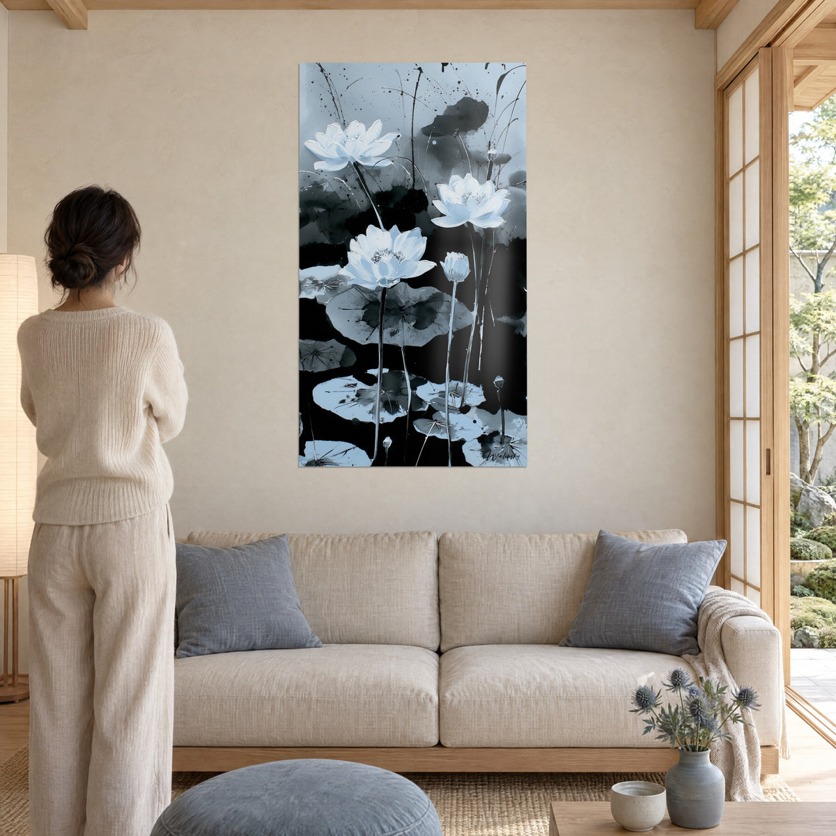 Quadro gigli d'acqua bianchi in piena fioritura su fondo grigio-azzurro con schizzi di inchiostro nero, donna di spalle, sopra un divano in un soggiorno luminoso