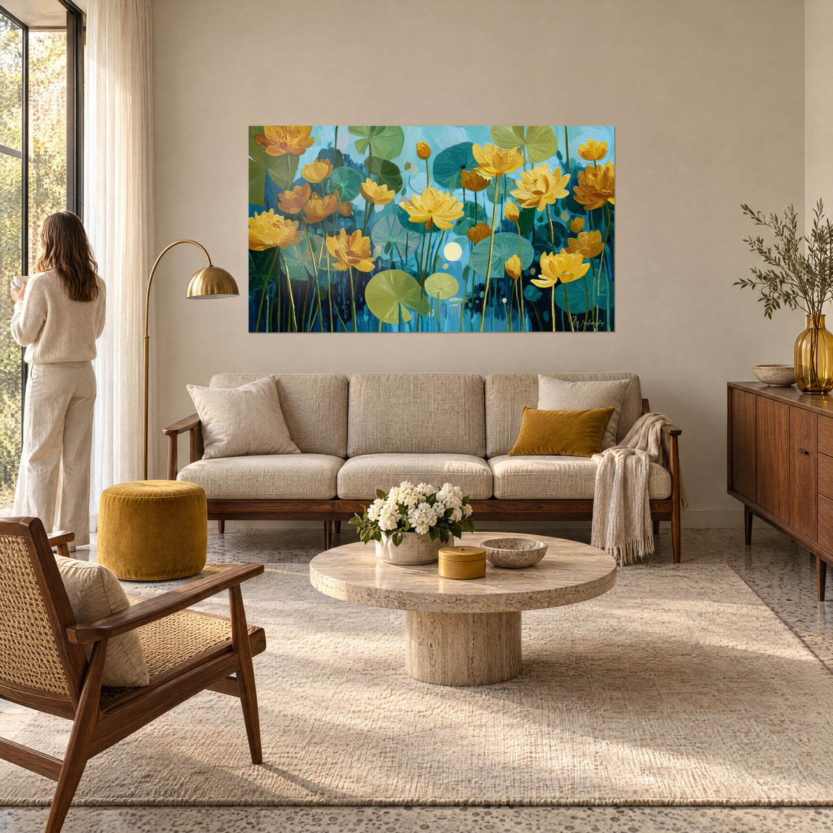 Quadro di ninfee dorate e foglie verde salvia su sfondo azzurro, donna di spalle, sopra un divano in un soggiorno luminoso