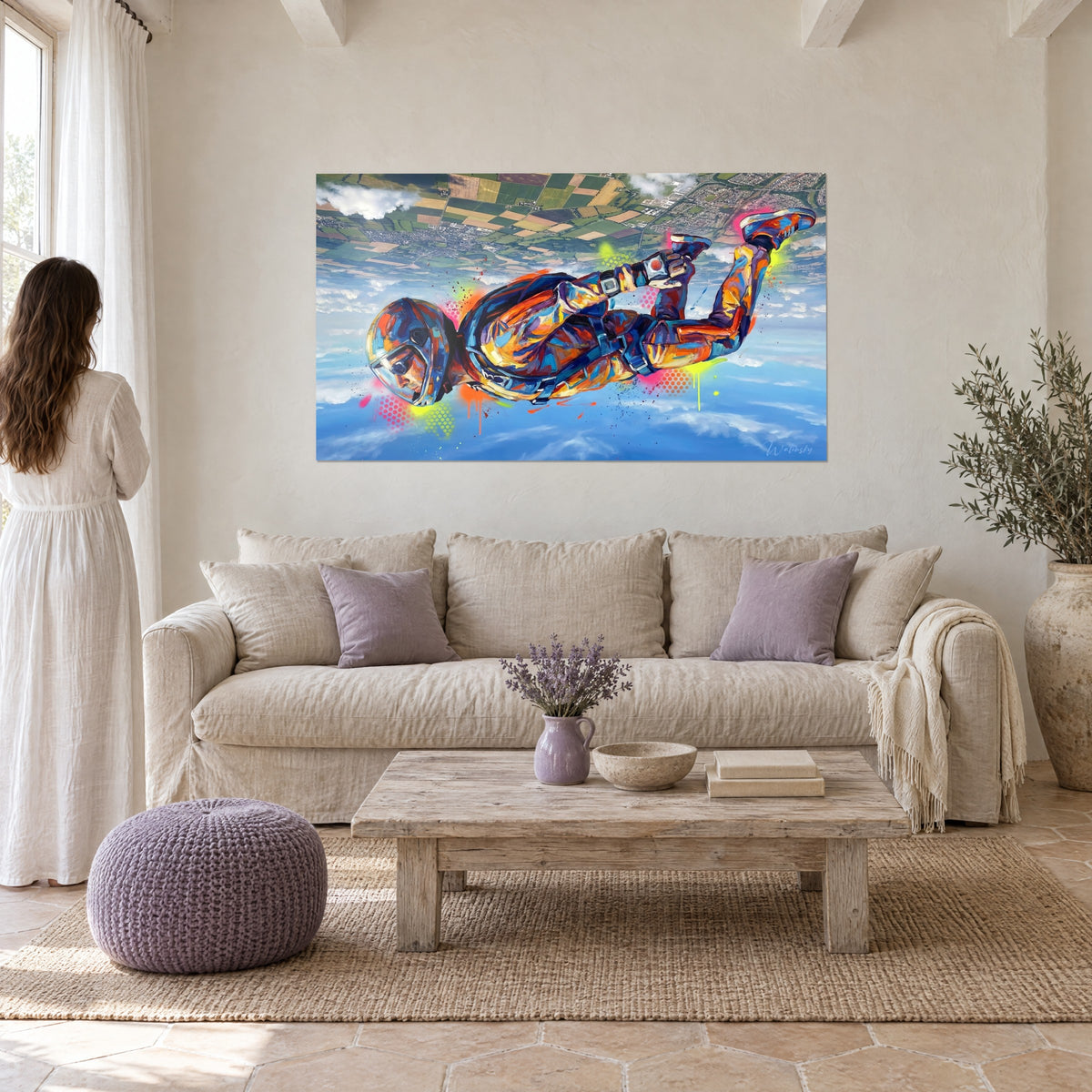 Gemälde eines Fallschirmspringers im freien Fall, orangefarbener und blauer Overall, grüne Felder im Hintergrund, über einem Sofa in einem hellen Wohnzimmer