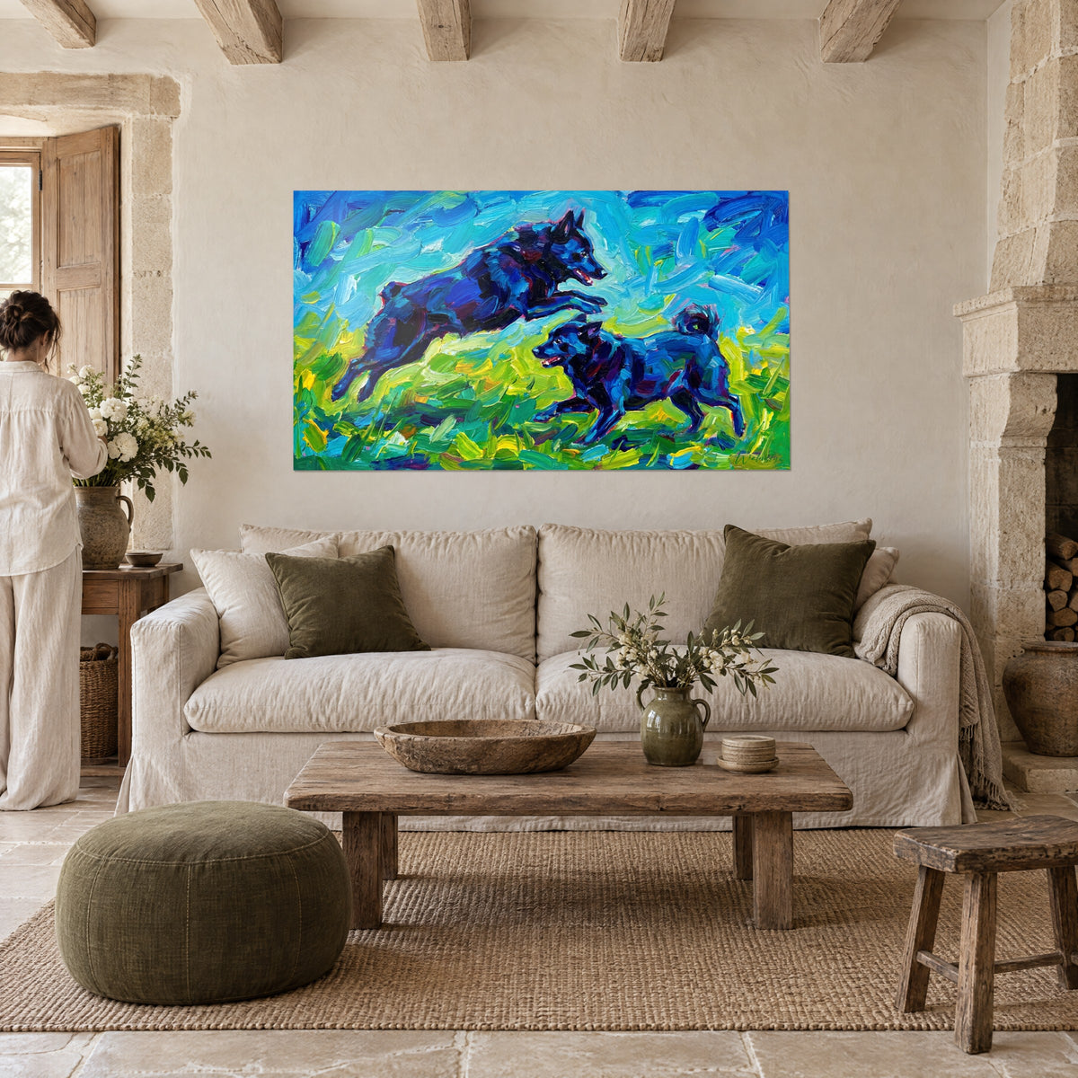 Wall art of a leaping black dog in cobalt blue and linden green, two women walking away from view, above a sofa in a bright living room