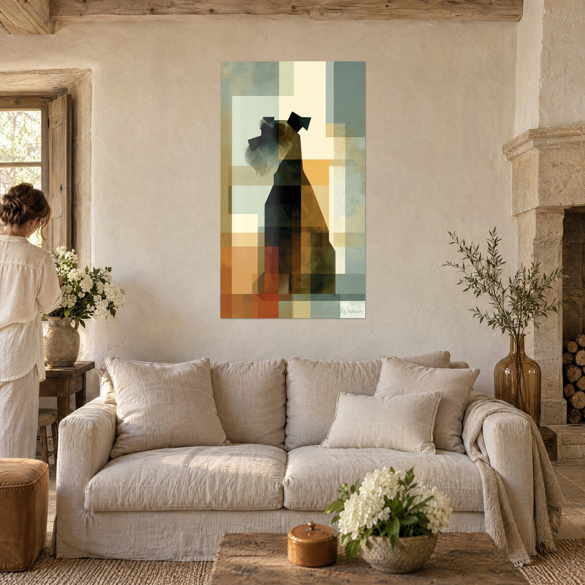 Tableau schnauzer assis en aplats géométriques ocre, noir et vert-de-gris, femme de dos, au-dessus d'un canapé dans un salon lumineux