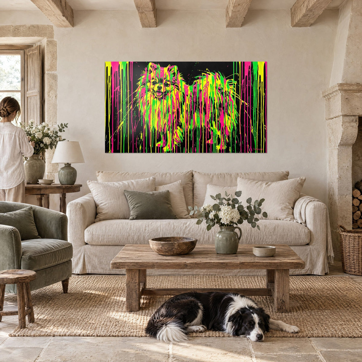 Wall art small spitz with tousled fur splattered with neon pink and lemon yellow drips on a black background, hung above a sofa in a bright living room