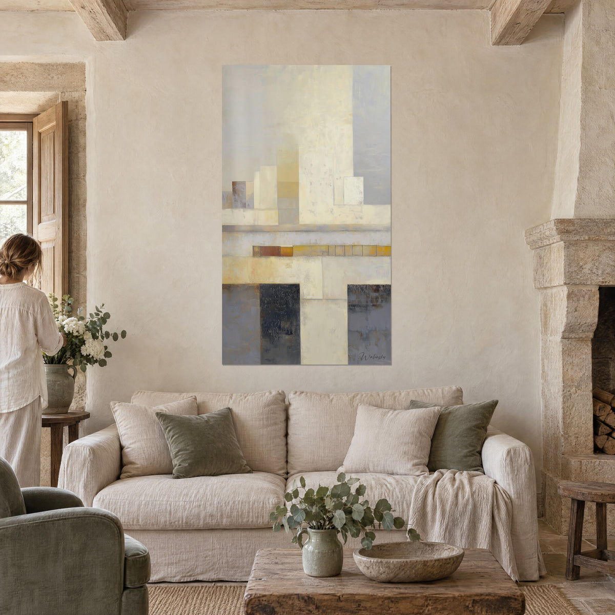Wall art geometric blocks in beige and pearl grey, ochre band at the centre, woman seen from behind, above a sofa in a bright living room