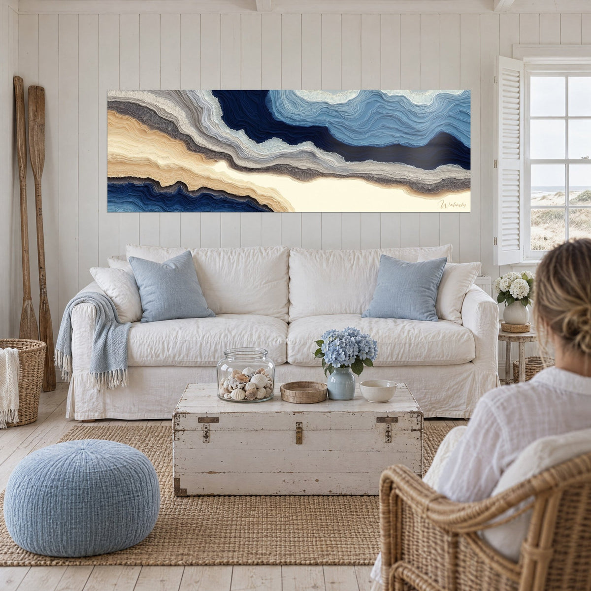 Cuadro con capas onduladas en azul océano y crema dorada, franjas grises, sobre un sofá en un salón luminoso
