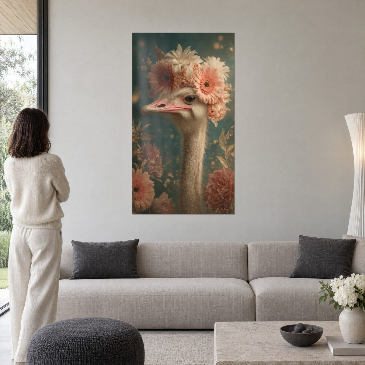 Wall art ostrich adorned with coral and cream gerberas on a blue-green background, woman seen from behind, above a sofa in a bright living room