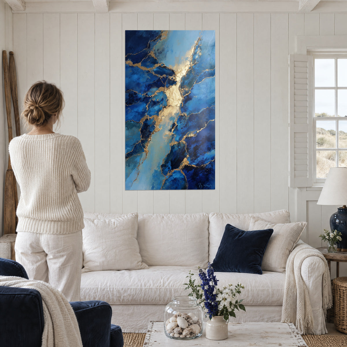 Gemälde aus blau-schwarzem Marmor mit goldenen Adern auf weißer Holztäfelung, Frau von hinten, über einem Sofa in einem hellen Wohnzimmer