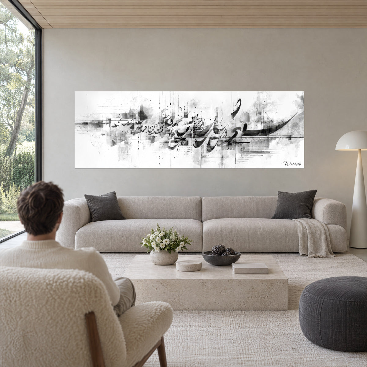 Wall art Arabic calligraphy in black and grey, ink strokes over an urban grid, back-facing silhouette above a sofa in a bright living room