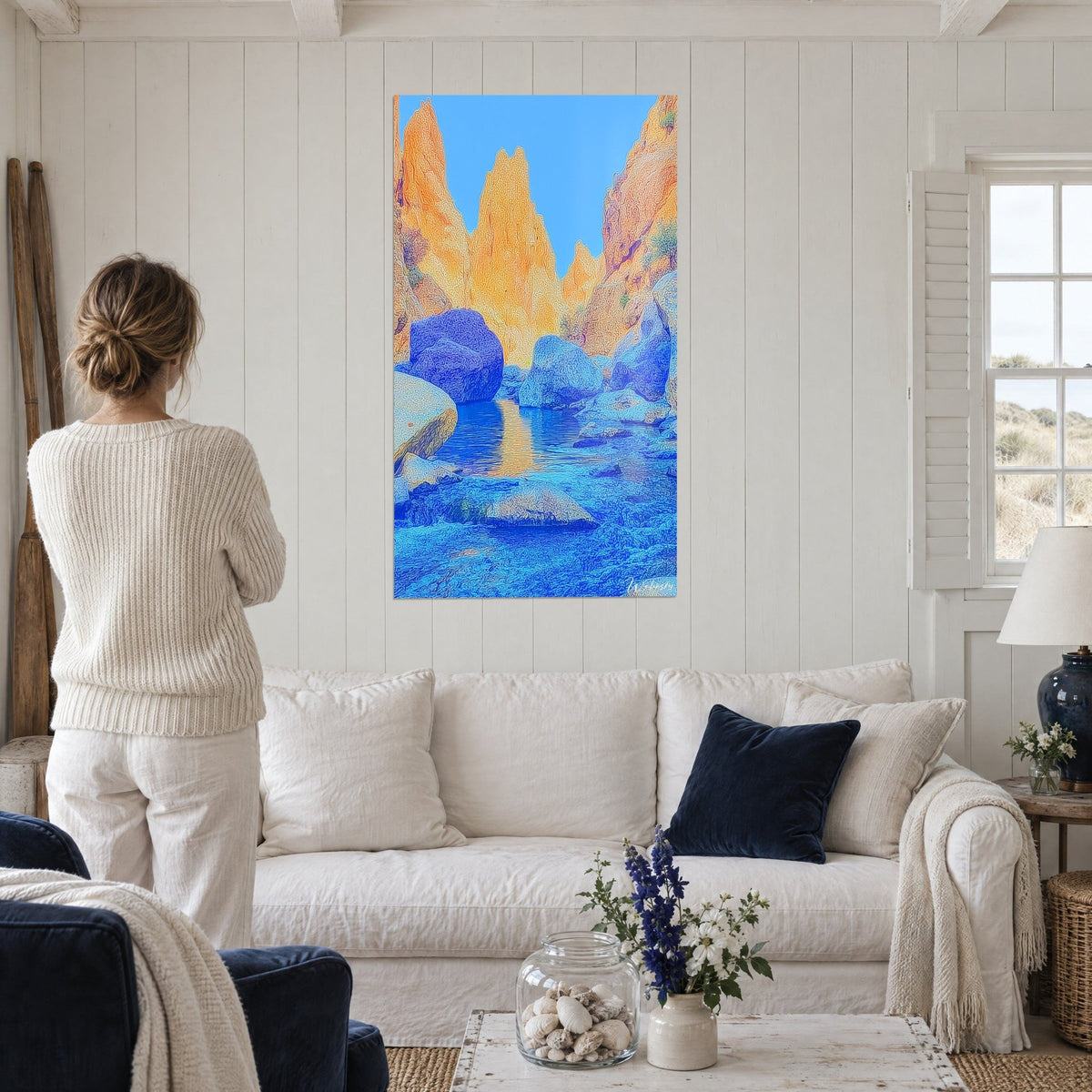 Wall art canyon with orange rock needles, cobalt blue water and azure sky, woman seen from behind, above a sofa in a bright living room