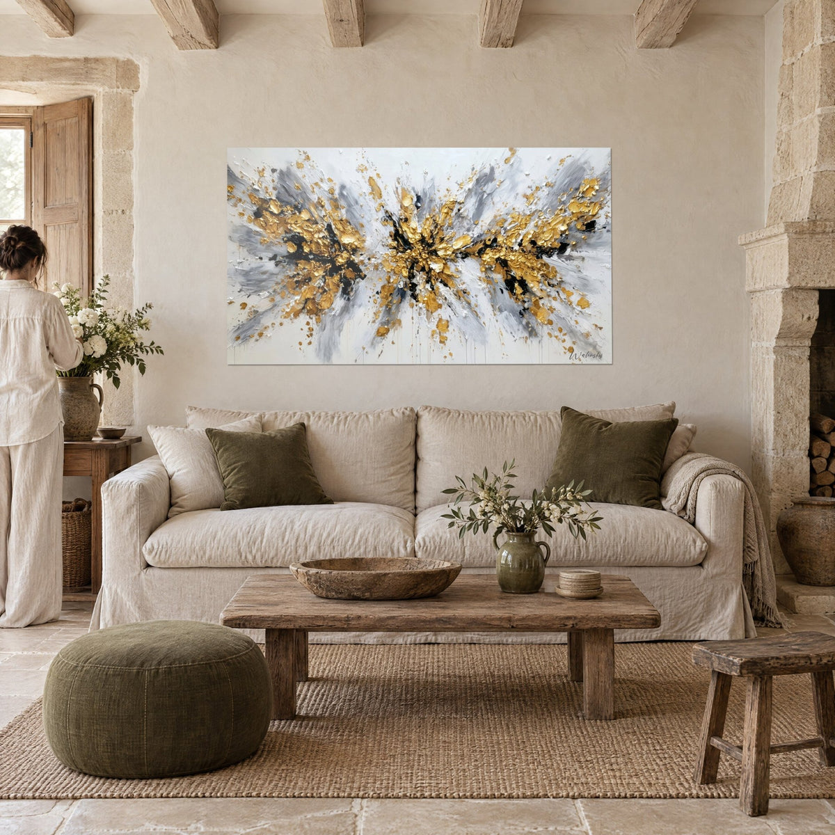 Tableau explosion de peinture dorée et grise sur fond blanc, accroché au-dessus d'un canapé dans un salon lumineux
