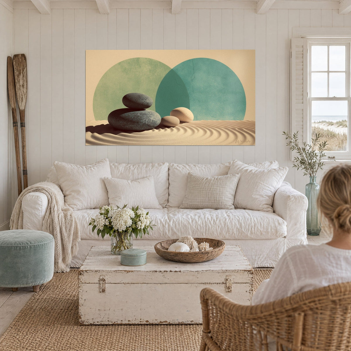 Gemälde mit aufeinandergestapelten grauen Kieselsteinen auf welligem Sand, zwei grüne und beige Kreise, über einem Sofa in einem hellen Wohnzimmer