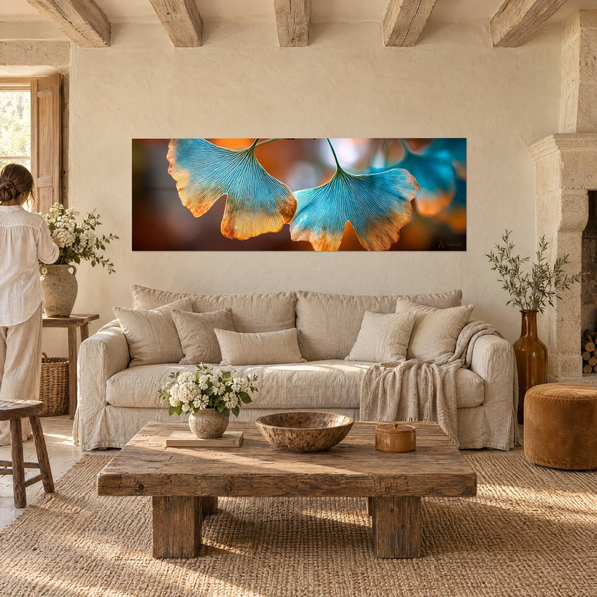 Wall art fan-shaped ginkgo leaves, golden veins on turquoise and orange, woman seen from behind, above a sofa in a bright living room