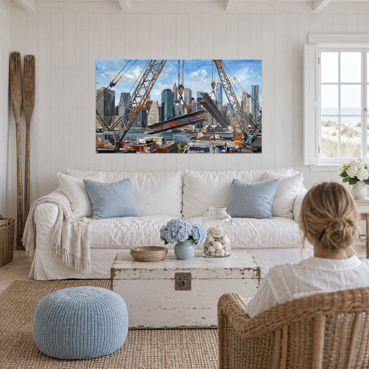 Wall art of rusted cranes and steel beams against blue skyscrapers, above a sofa in a bright living room